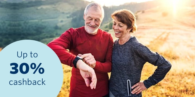 An elderly couple out on a hike on a sunny day as they look at the husband's smartwatch.