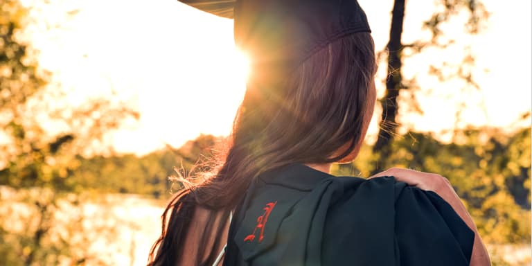 A young girl in her graduation gown walking among trees.