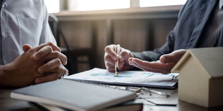 The hands of two people over a desk with notebooks and papers, having a meeting.