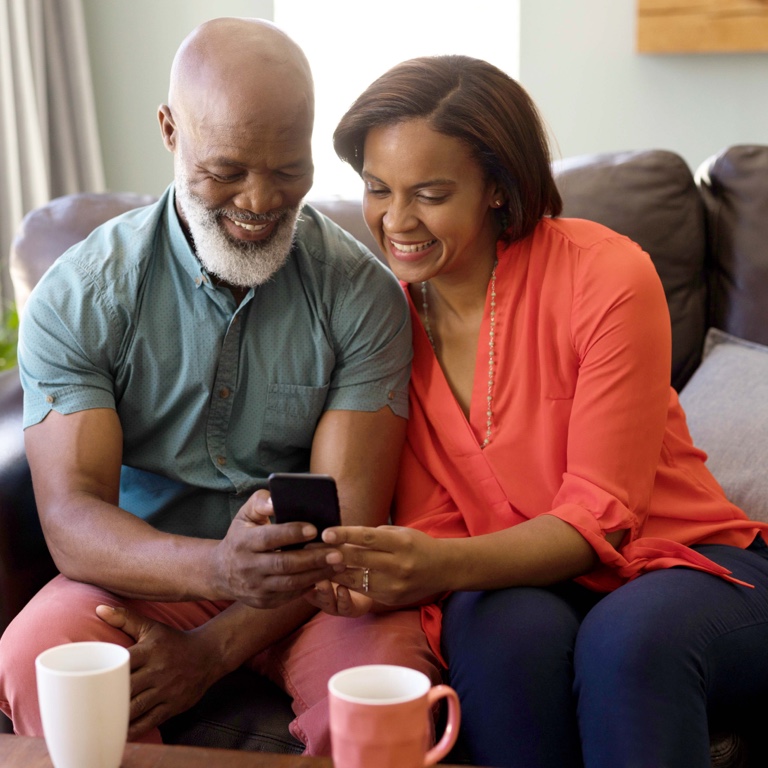 A middle-aged couple looking into phone a screen and smiling.