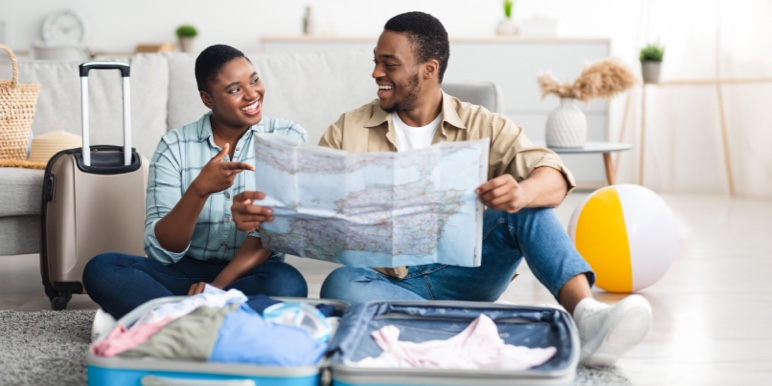 A young African couple looking at a paper map, smiling confidently that they have all their items packed and itinerary planned for their December holiday.