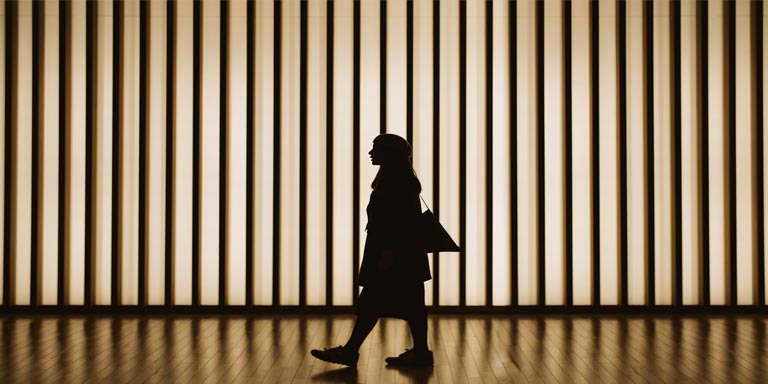 The silhouette of middle-aged woman with a big handbag, walking inside a building.