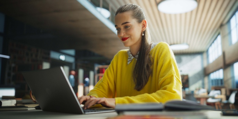 A smilling young digitally savvy woman in a yellow jersey, drafting a free Will on her laptop using the Momentum Trust online Wills platform.