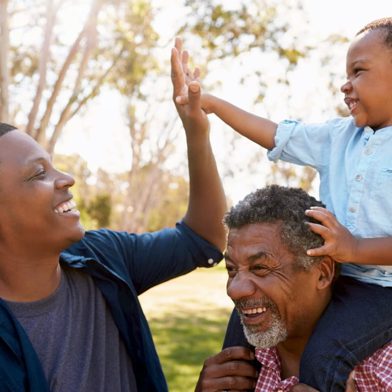 A retired man at a park with his grandson on his sholder giving his father a high-five.