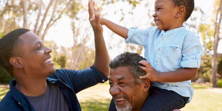 A retired man at a park with his grandson on his sholder giving his father a high-five.