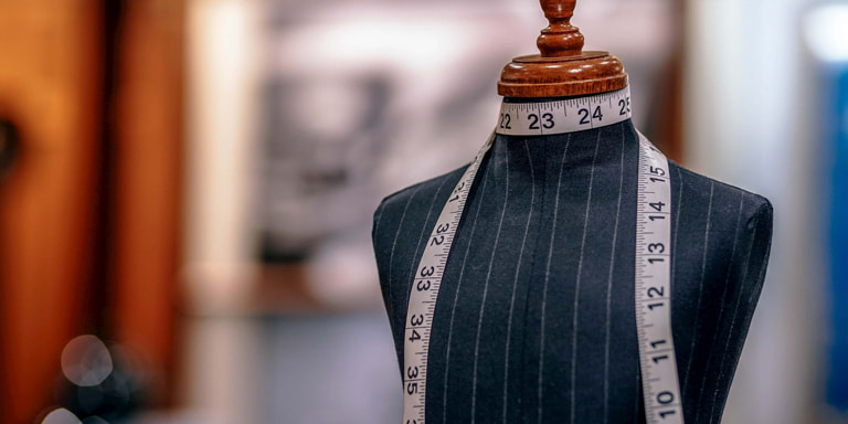 A black and white stripped manikin with a measuring tape wrapped around its neck. It has no arms and head.