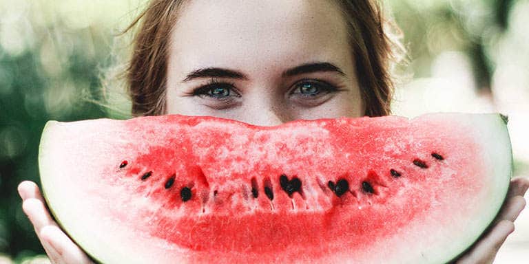 A young female holds up a ripe watermelon quarter in place of her smile.