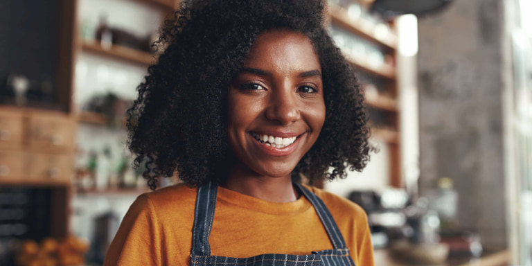 Young black lady wearing a mustard top and blue pinstripe apron smiling as she is covered with Momentum Health4Me.