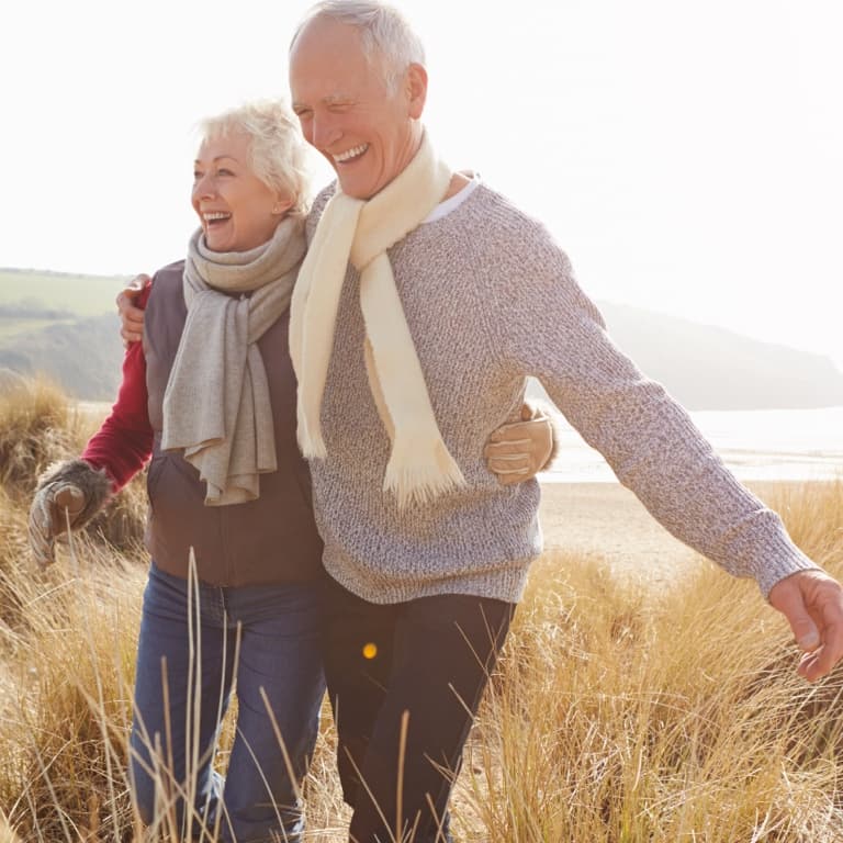  A happy elderly couple in scarfs walking in a field of dry grass.