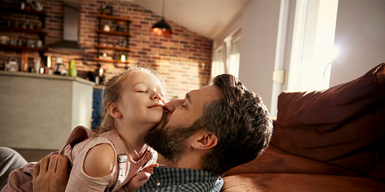 A happy young father embracing his young daughter, sitting on the floor of their home, showing gratitude that all his belongings are insured.