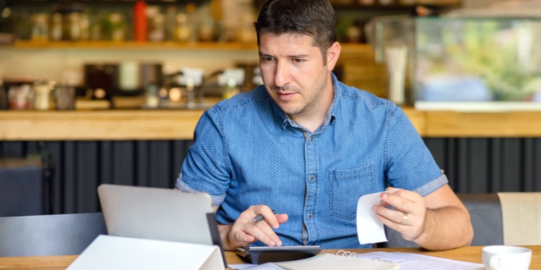 Concerned man sitting looking at receipts while using a calculator.
