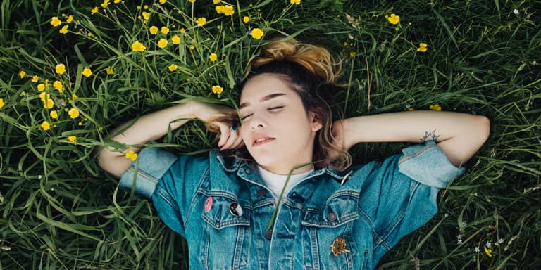 A lady sleeping in a bed of little yellow flowers wearing a denim shirt.