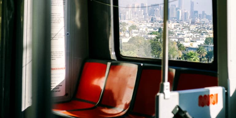 Two empty orange train seats and a window above them, with a view of a city.