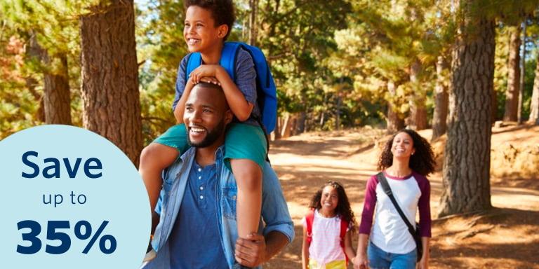 Young mom and dad are walking in the park. The dad is carrying his son on his shoulders.