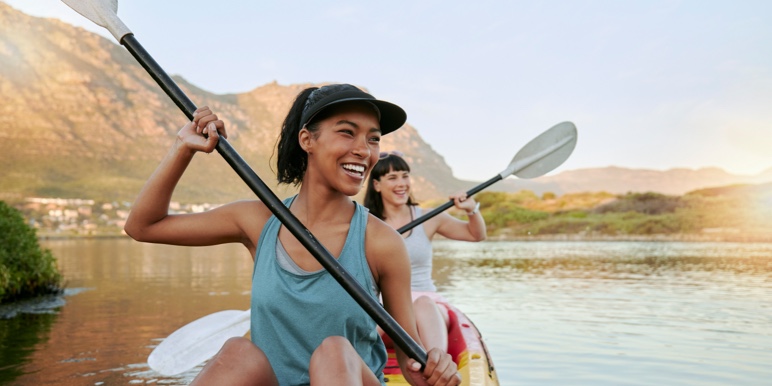 A rowing team of two happy women rowing a canoe together in a lake.