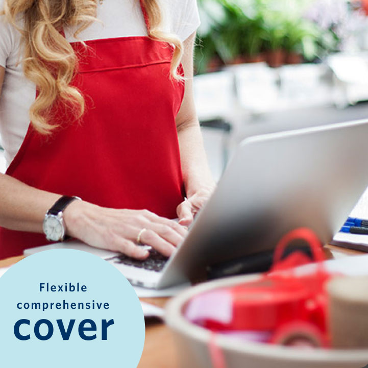 A female business owner wearing a red apron working on a laptop at a retail or small business setting. Her business is covered with flexible comprehensive cover from Momentum Insure's business insurance.