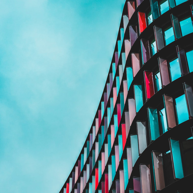 A modern multistory office building made with multi-colured glass in different shades of reds and blues, against a blue sky drop.