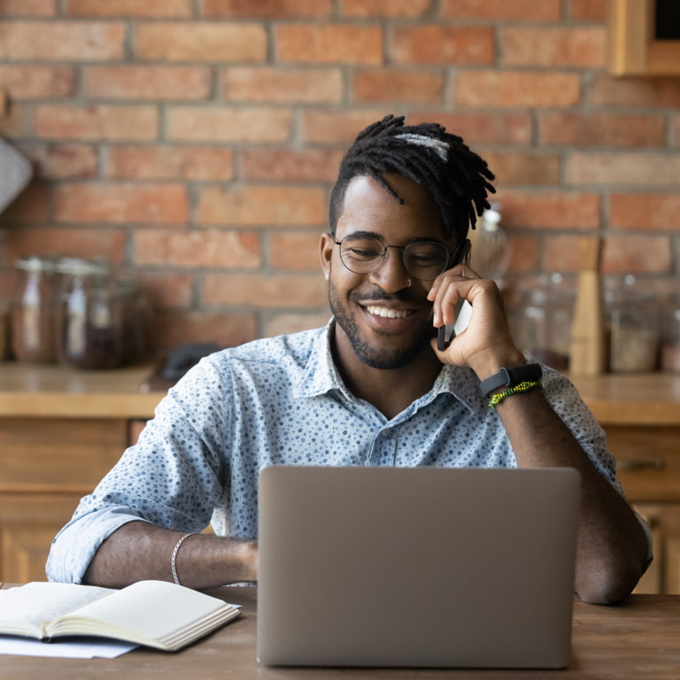 A man sitting at a desk is on the phone and smiling as he completes his free online will on his laptop.