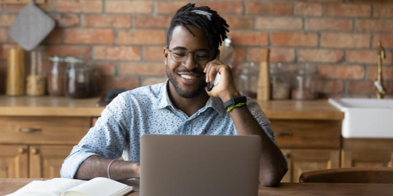 A man sitting at a desk is on the phone and smiling as he completes his free online will on his laptop.