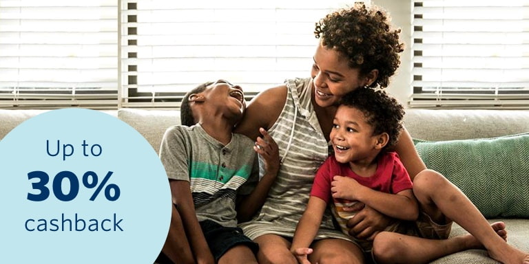 A young mother sitting on a couch and cuddling her two young toddlers, happy and confident that all her belongings are insured with a 30% cashback benefit.