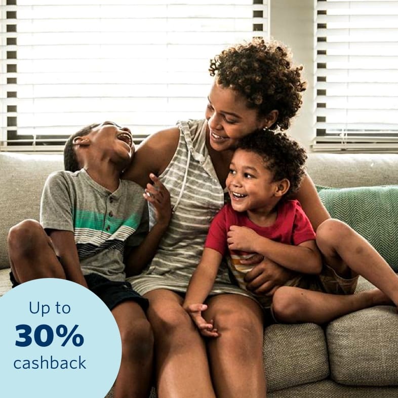 A young mother sitting on a couch and cuddling her two young toddlers, happy and confident that all her belongings are insured with a 30% cashback benefit.