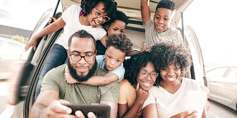 A family of 7 sitting in their SUV boot relieved about help on the way from a responder after using the Safety Alert feature's panic button that is free of charge for Momentum Insure short term insurance policyholders.