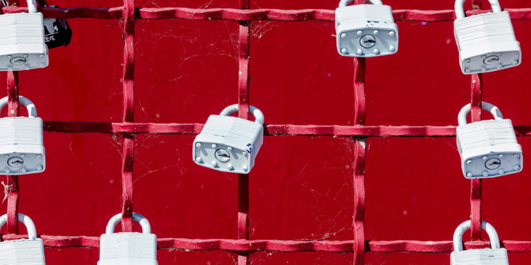 Red grid wire fence with nine white heavy duty padlocks fastened on numerous grids.