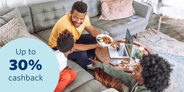 A happy young family sitting in their living area accessing their 30% cashback benefit on a laptop and feeling safe and secure that all their belongs are insured.