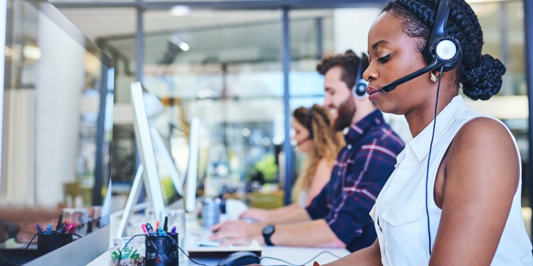 Call center staff, sitting at their work stations with their headphones on, attending to client phone calls.