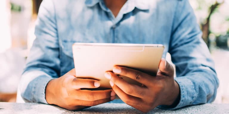 A close up of a man holding a tablet, wearing a blue shirt while going through FundsAtWork's digital tools.