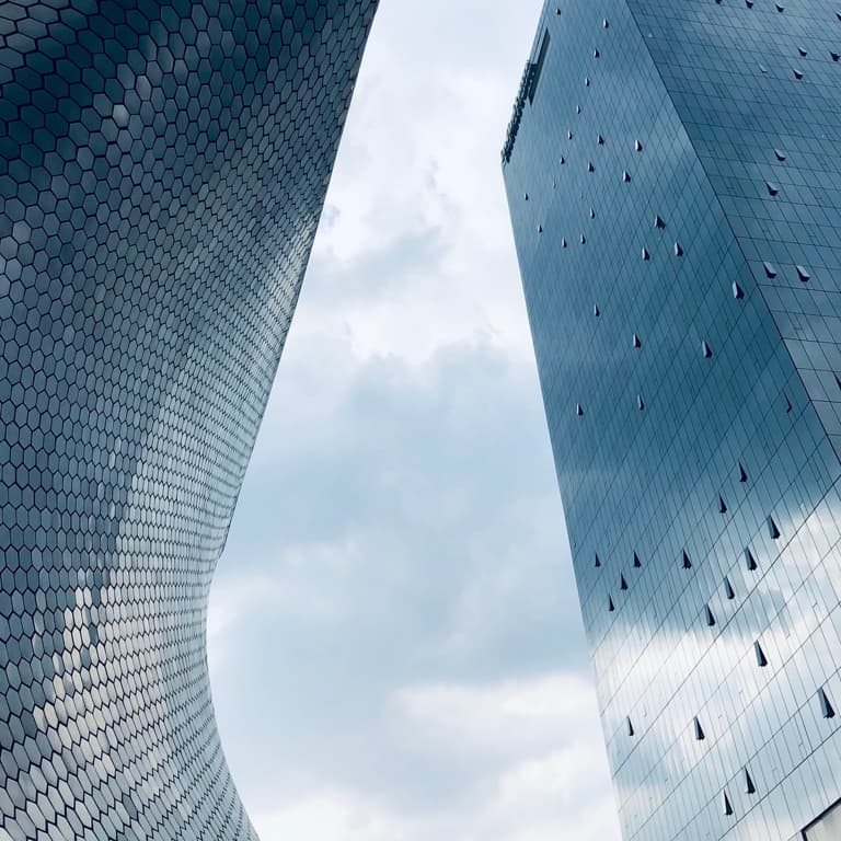 Two tall buildings facing each other where you can see a stormy sky. The building on the left has hexagonal-shaped windows while the building on the right has large rectangular windows.