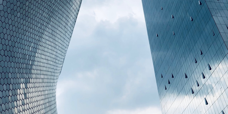 Two tall buildings facing each other where you can see a stormy sky. The building on the left has hexagonal-shaped windows while the building on the right has large rectangular windows.