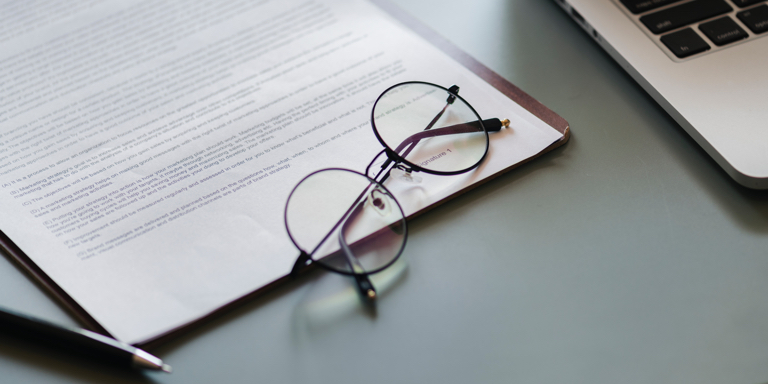 Reading glasses placed on an unsigned Will document with a pen next to it and an open laptop.