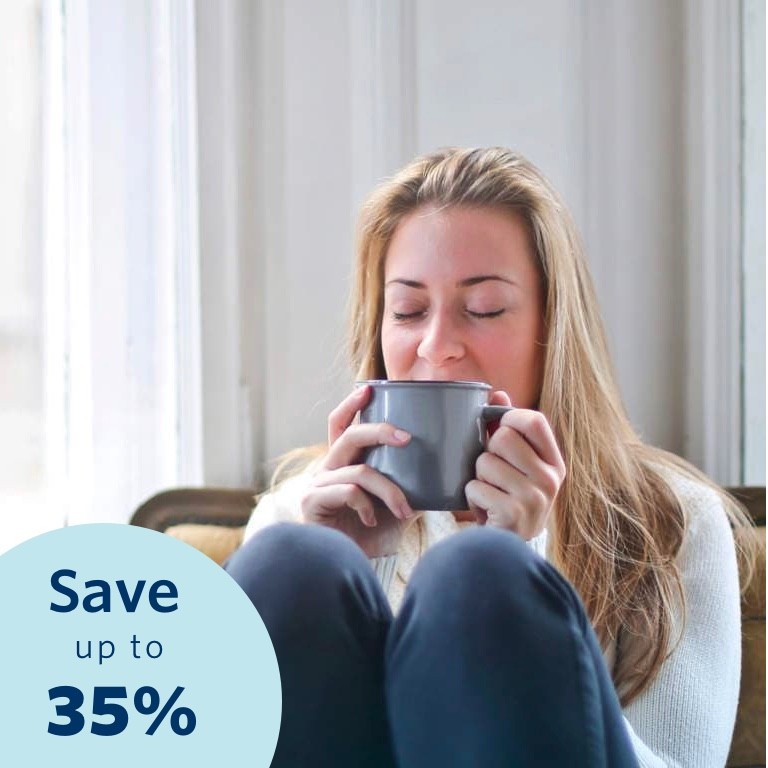 Young blonde woman with her eyes closed relaxing on a chair in her home, drinking a cup of coffee.