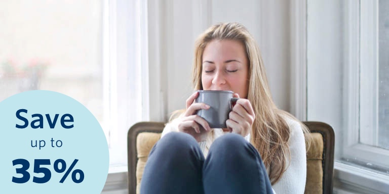 Young blonde woman with her eyes closed relaxing on a chair in her home, drinking a cup of coffee.