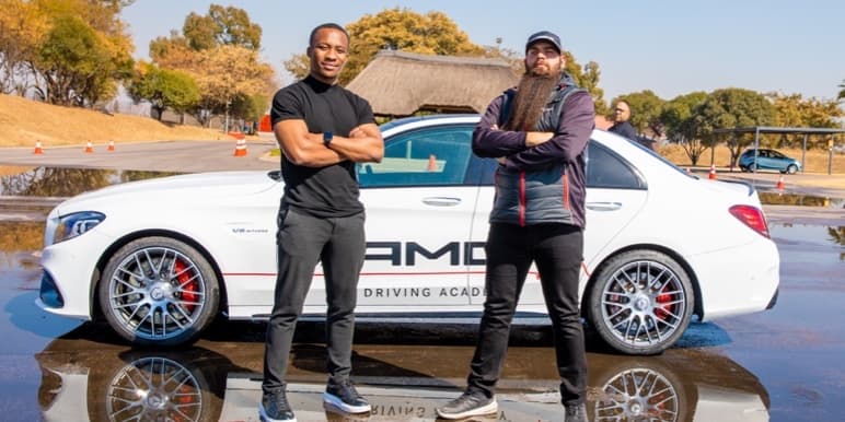 Zamani Mbatha and his driving instructor standing in front of a white Mercedes AMG on a wet road about to conquer his fear of driving in the rain.