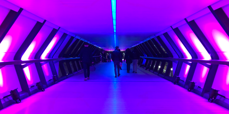 A group of investment specialists walk through a corridor illuminated by pink and blue lights.